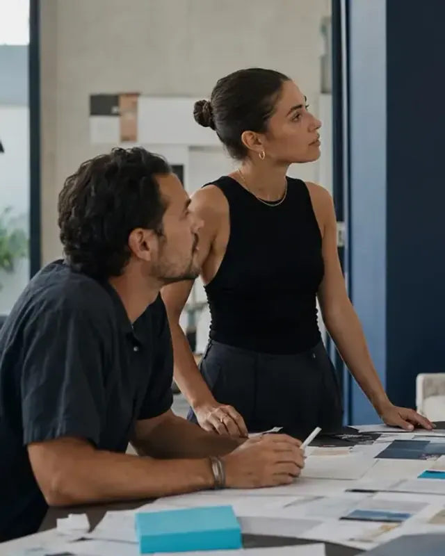 Two Mind Miami strategists listening in a working session, notes and swatches spread across the table